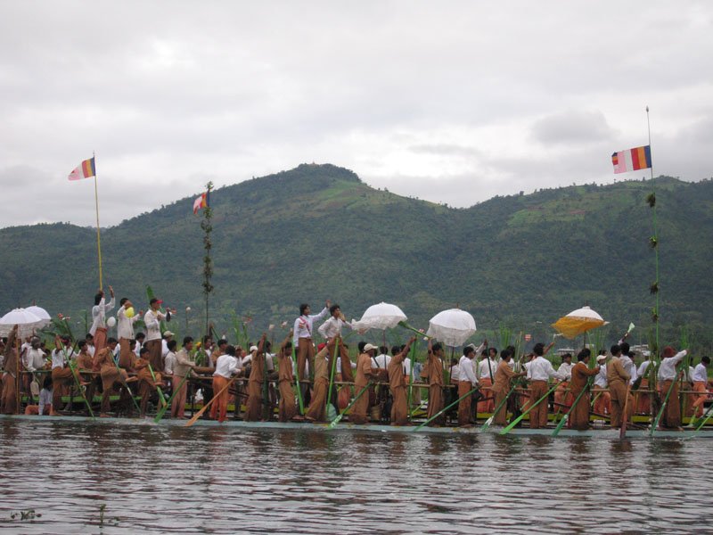 the men standing on the elevated pole in the middle of this slender boat are singing and dancing

