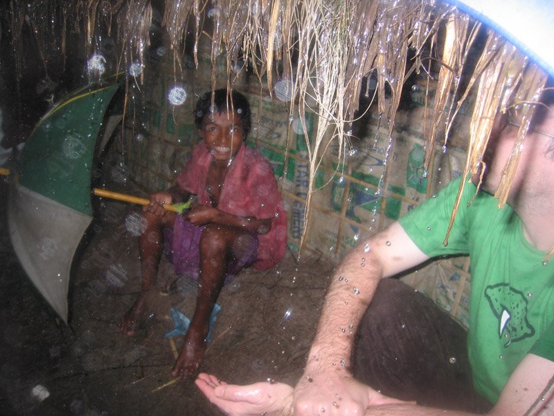 after we had lunch, we (Chuck & Anika) went for a walk on the beach. then the skies opened up and it started pouring, sheets of rain. here is Chuck and a local burmese-speaking boy huddling under the overhang of a thatched house.
